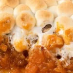 Sweet potato casserole topped with marshmallows and pecans, served in a dish.